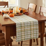 Sage & Mustard Plaid Table Runners draped over a wooden dining table, featuring a pattern of sage green, mustard yellow, putty brown and white intersecting stripes.