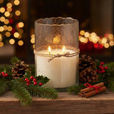 Artisan Clear Bubble Glass Hurricane Hand-Poured Soy Scented Candle in a textured clear glass vessel sits on a wooden surface surrounded by pine branches, holly leaves, red berries, pinecones, and cinnamon sticks, with warm blurred holiday lights in the background. The candle has a paper label reading Himalayan.