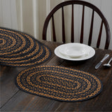 Blackstone Farm Braided Oval Placemat Set of 6 –12x18 – Black and Tan Jute on a dark wood dining table, styled with a white bowl and plate, silverware with a wooden chair.