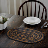 Blackstone Farm Braided Oval Placemat Set of 6 –10x15 – Black and Tan Jute on a dark wood dining table, styled with a white bowl and plate, silverware, and plant arrangement with a wooden chair.