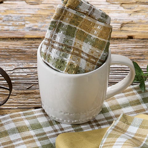 White mug with Sage & Mustard Dishcloth inside, on a wooden surface with a checkered cloth.