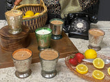 Fleur de Lys Tumbler Hand-Poured Soy Scented Candles with patterned silver, green, and clear glass are arranged on a table with lemons, strawberries, a basket, and a black rotary telephone in a styled indoor setting