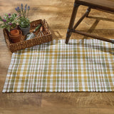 Sage & Mustard Plaid Chindi Rag Rug on a wooden floor with a basket of plants.