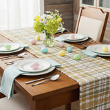 Sage & Mustard Plaid Chindi Table Runners draped over a wooden table, featuring a plaid pattern in sage green, mustard yellow, putty brown and white.