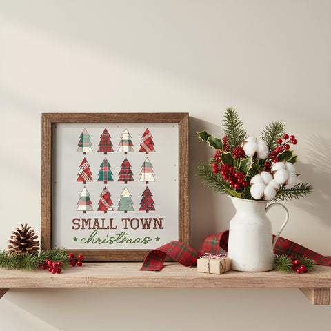 Small Town Christmas wood sign in rustic brown frame on a farmhouse shelf with a white pitcher of holly, red berries, pinecone, plaid ribbon, and a small gift box