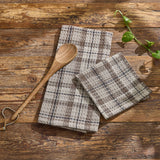 Two Tinderbox Brown Plaid Waffle Dishtowels stacked and folded on a rustic wood farmhouse surface with a wooden spoon and fresh basil — 100% cotton waffle weave dishtowels in brown and oatmeal plaid, set of 2